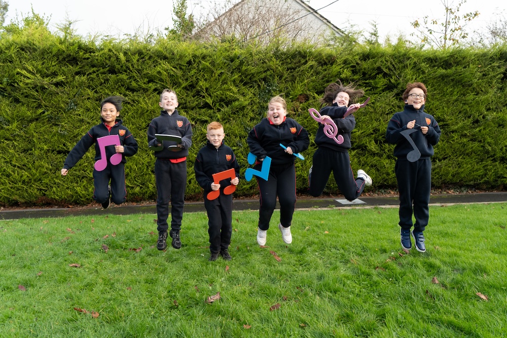 A group holding cut out musical notes and jumping in the air whilst looking happy